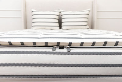 A view of the foot of a bed made with white and black striped zipper bedding with a focus on the two zippers.
