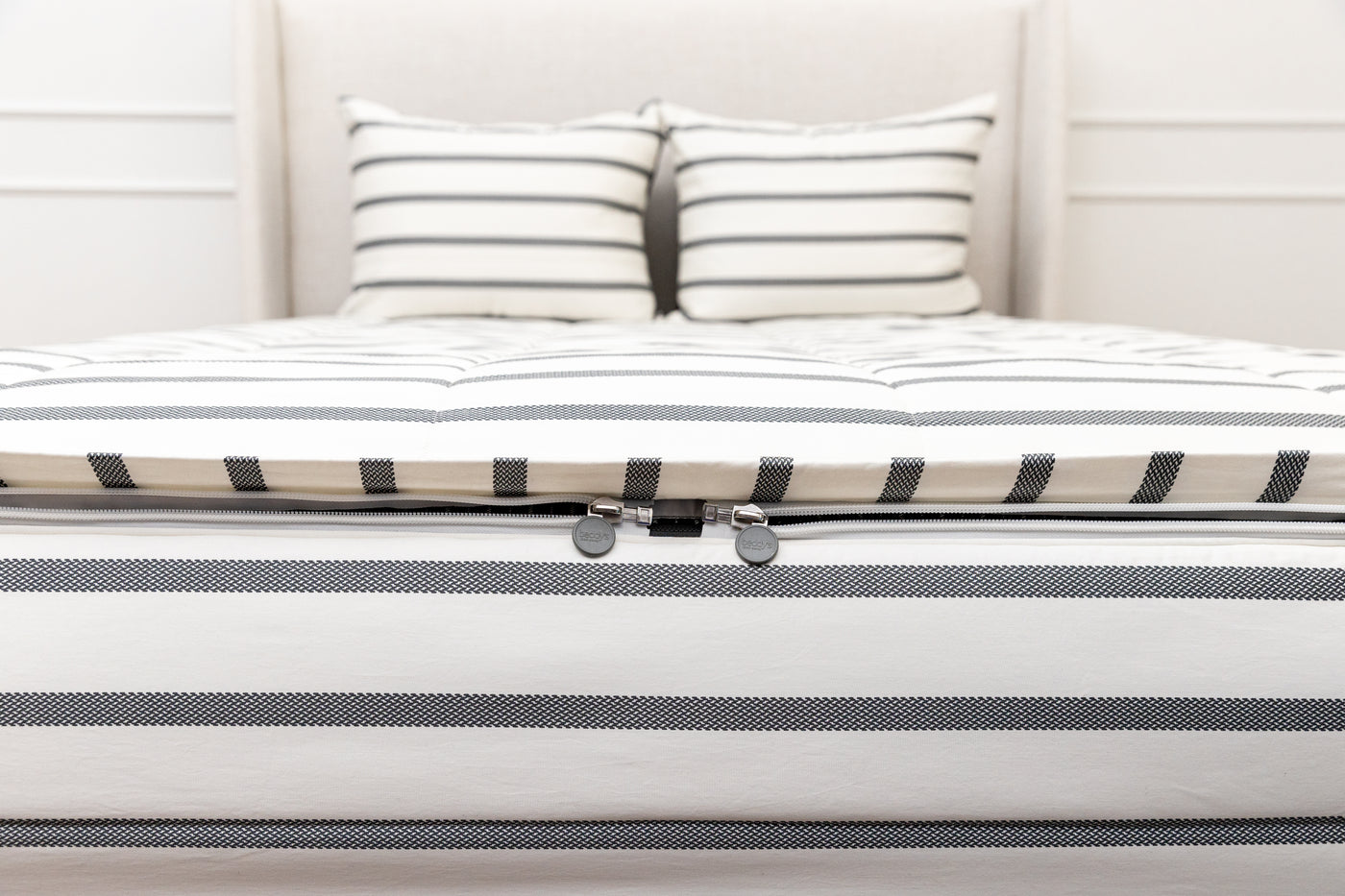A view of the foot of a bed made with white and black striped zipper bedding with a focus on the two zippers.