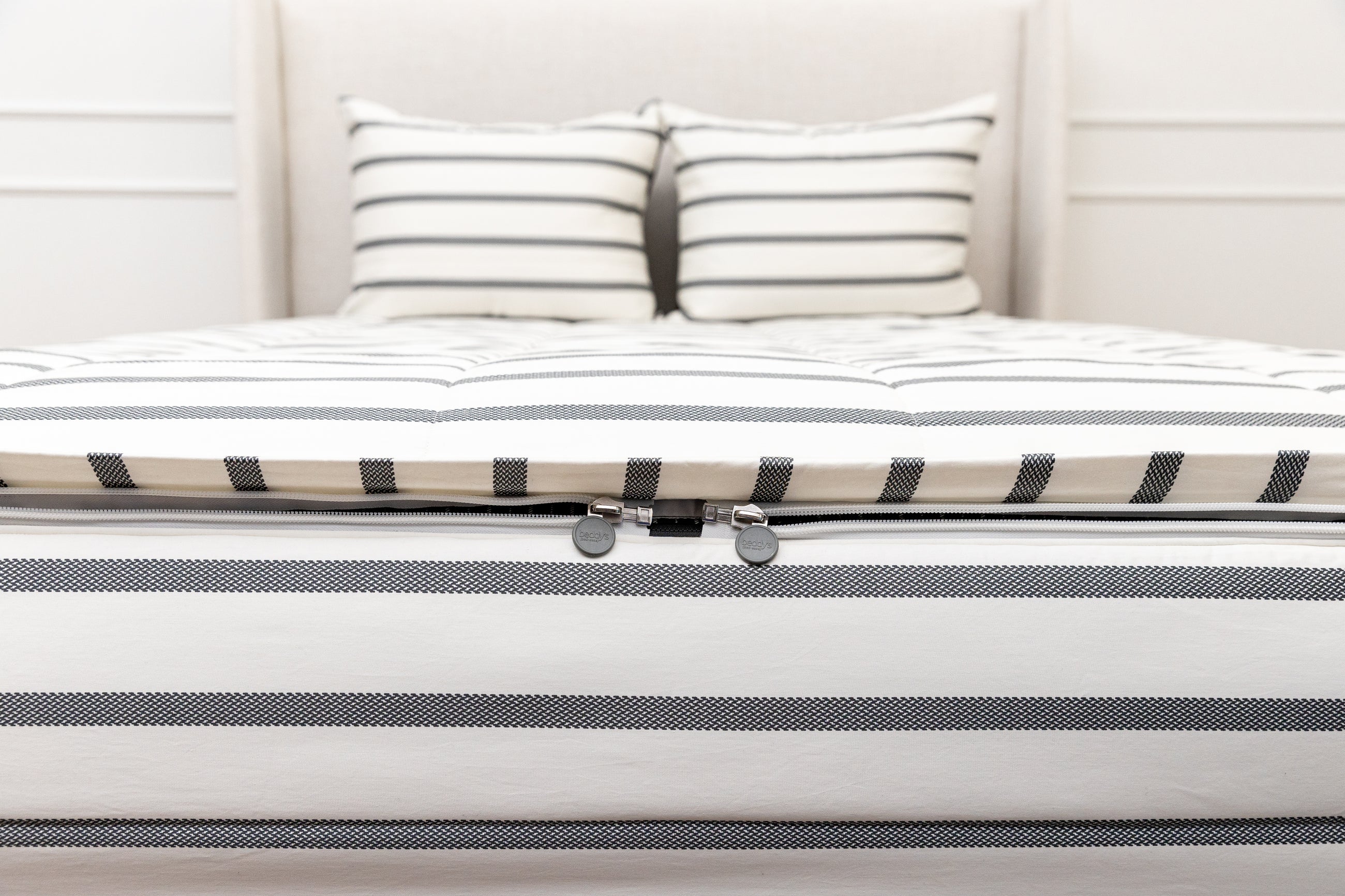 A view of the foot of a bed made with white and black striped zipper bedding with a focus on the two zippers.