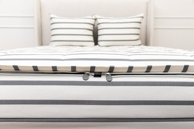 A view of the foot of a bed made with white and black striped zipper bedding with a focus on the two zippers.