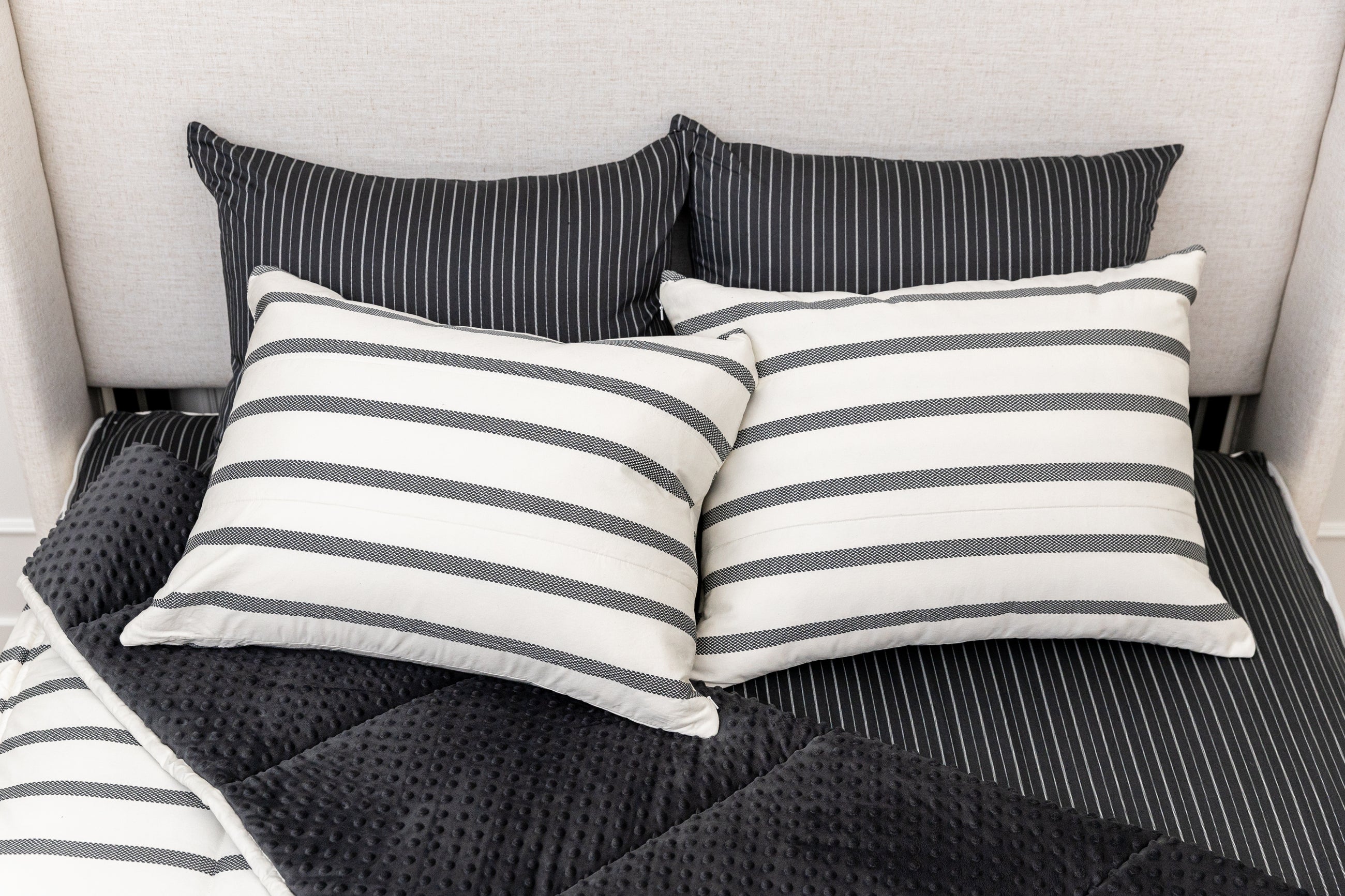 A bed made with white and black striped zipper bedding with the top pulled back to reveal the inside lining, and four pillows arranged on top