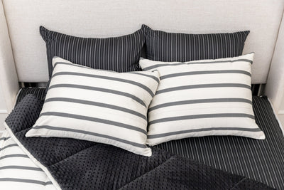 A bed made with white and black striped zipper bedding with the top pulled back to reveal the inside lining, and four pillows arranged on top