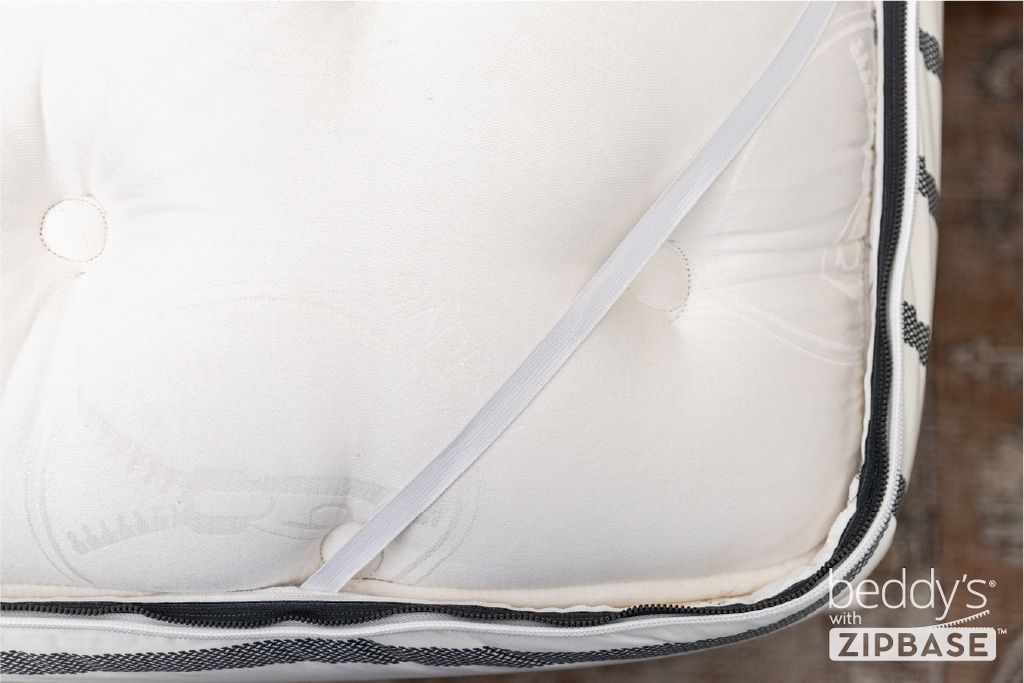 A close up shot of a zipper bedding set with ZipBase with the inside sheet unzipped and pulled back to reveal the elastic.