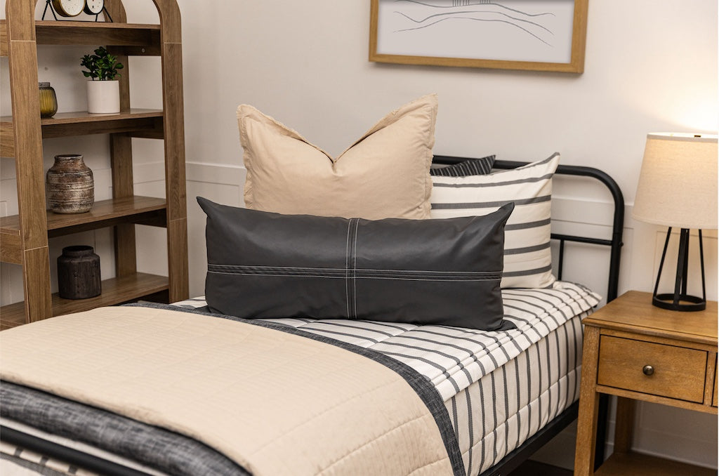 A twin bed made with white and black striped zipper bedding paired with neutral tan and black accessories.