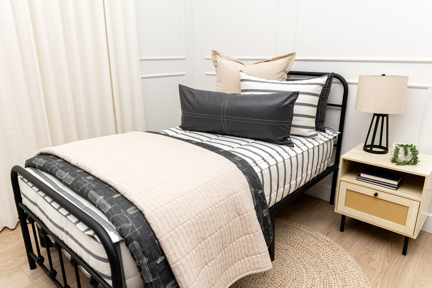 A twin bed made with white and black striped zipper bedding paired with neutral tan and black accessories.