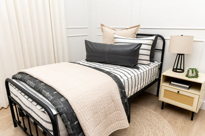 A twin bed made with white and black striped zipper bedding paired with neutral tan and black accessories.