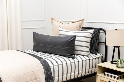 A twin bed made with white and black striped zipper bedding paired with neutral tan and black accessories.