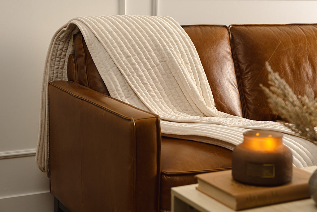 A cream chenille and minky blanket set on an orange leather couch. 