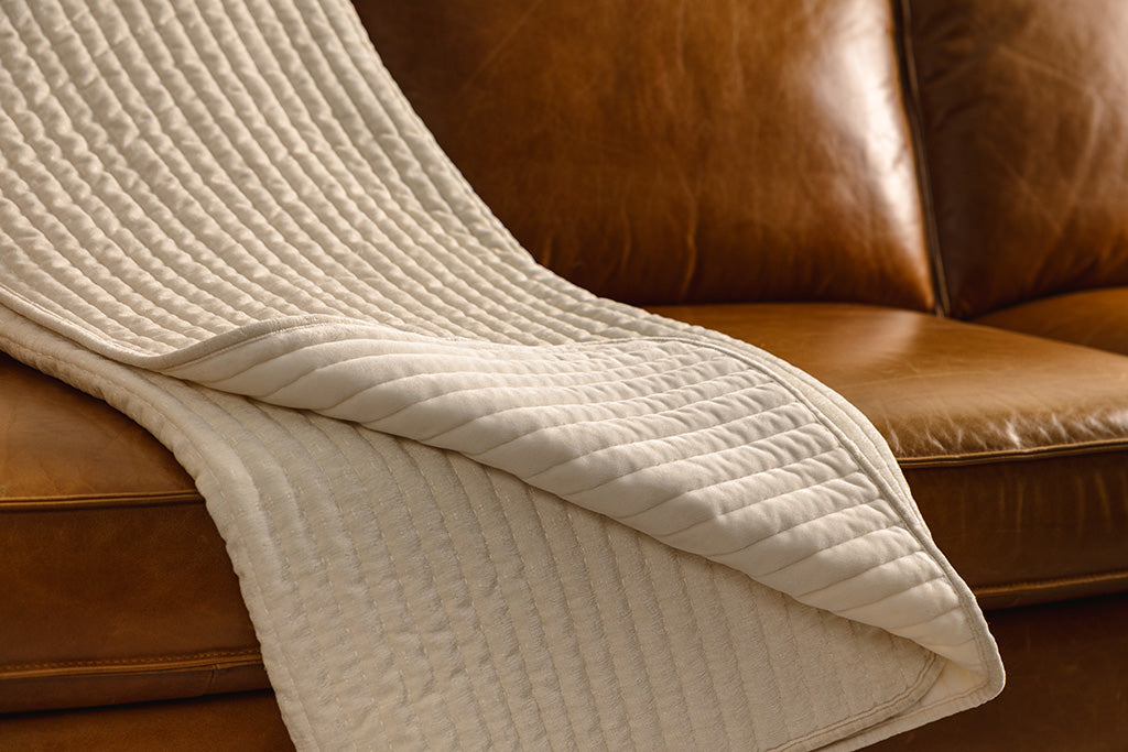 A cream chenille and minky blanket on an orange leather couch.