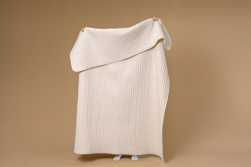 A model holding a cream chenille and minky blanket on a tan backdrop.