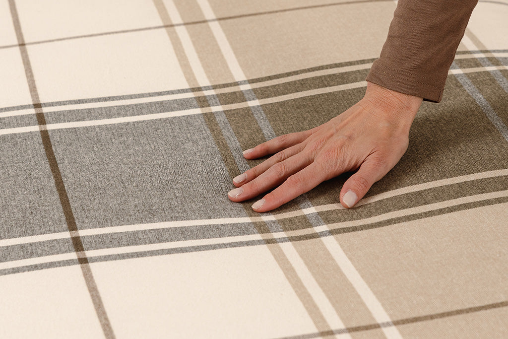 A woman running her hand on a brown, gray, and white plaid duvet.