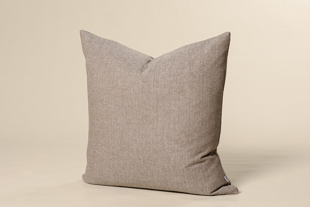 A brown woven pillow on a cream paper backdrop.