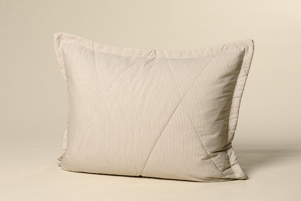 A white and tan striped quilted sham on a cream backdrop.