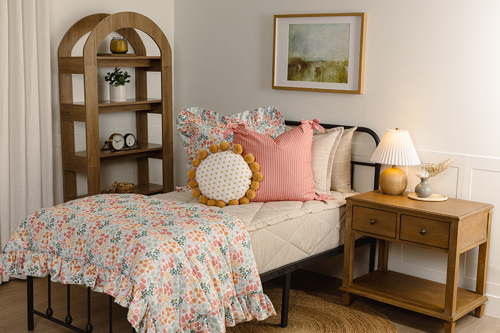 A twin bed with tan stripe quilted bedding with floral, pink stripe, and yellow accessories. 