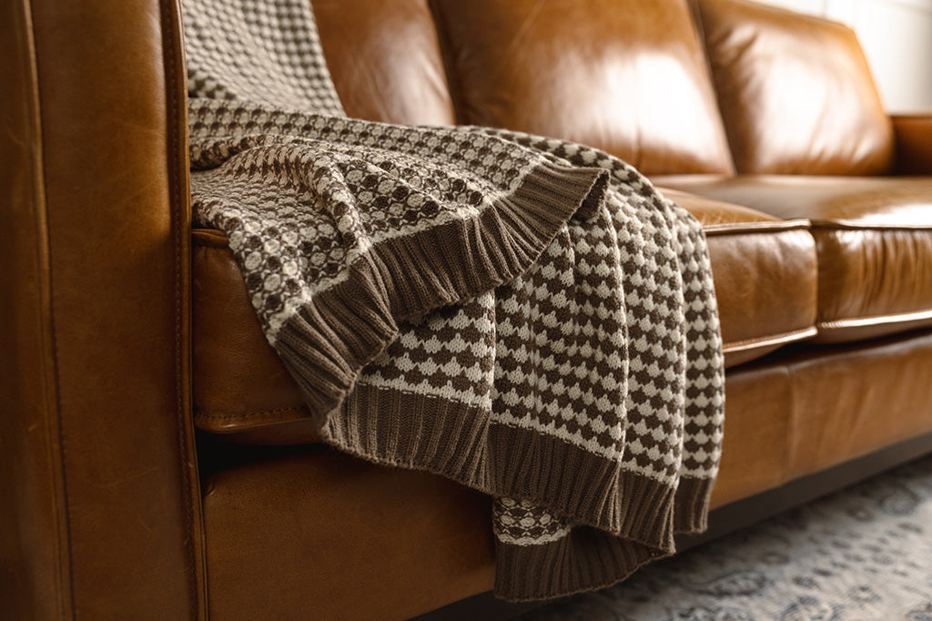 A brown and cream scallop weave throw on an orange leather couch.