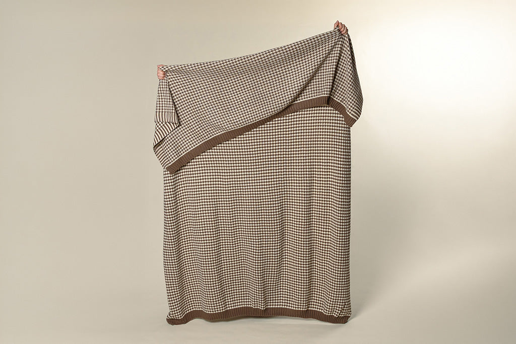 A brown and cream scallop weave throw on a paper backdrop.