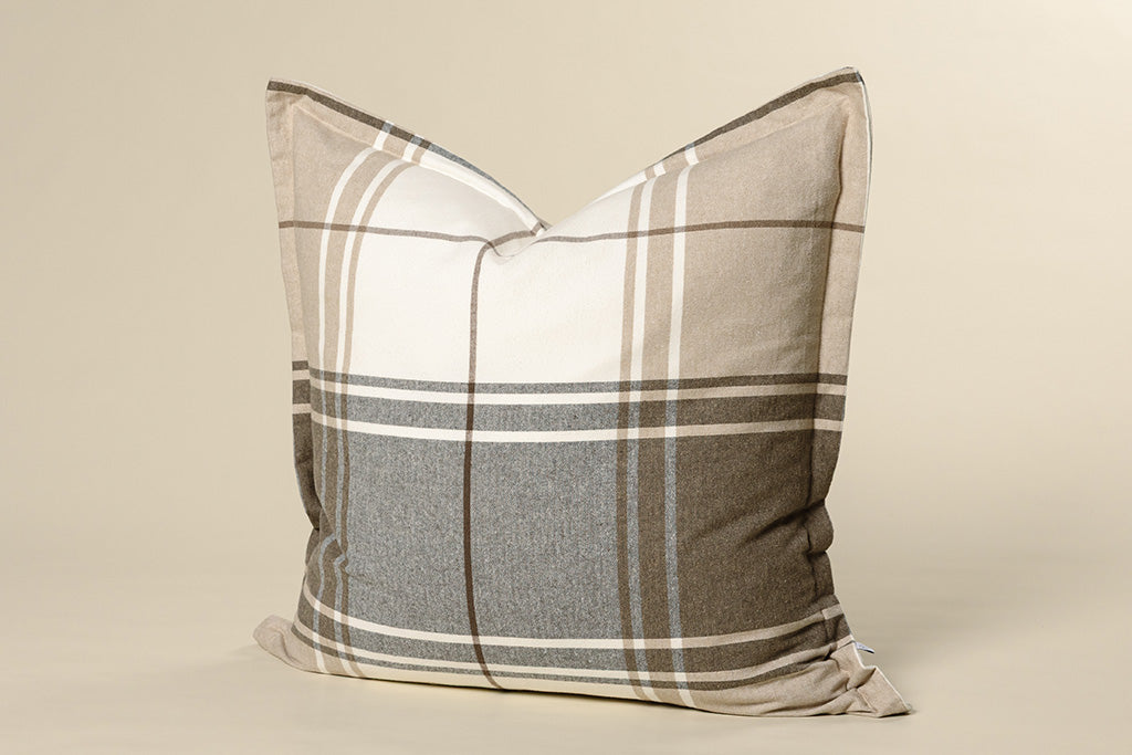 A brown, gray, and white plaid pillow on a cream paper backdrop.