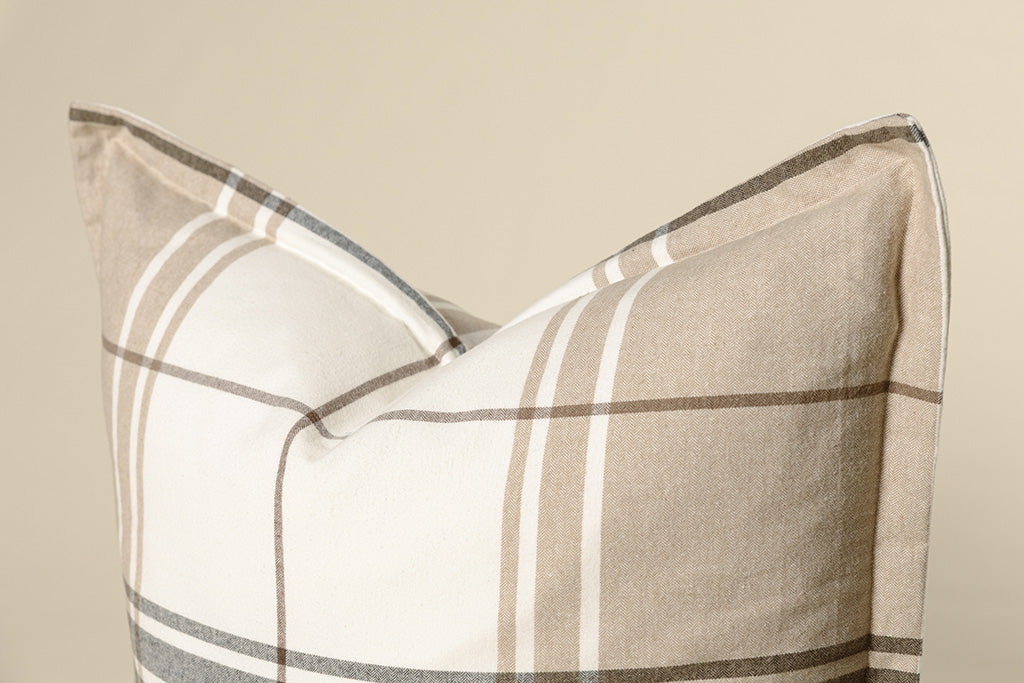 Close-up shot of a brown, gray, and white plaid pillow on a cream paper backdrop.