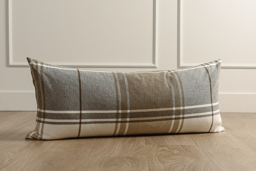 Brown, gray, and white xl lumbar pillow on wood floor with a wainscoting background.