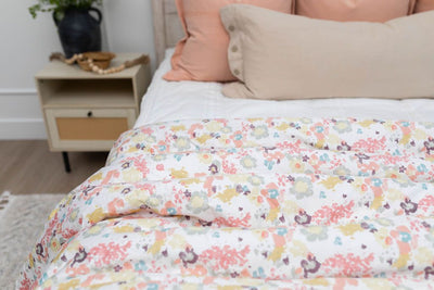 A close up of a bed made with white zipper bedding and neutral and peach pillows and a colorful floral pattern blanket.