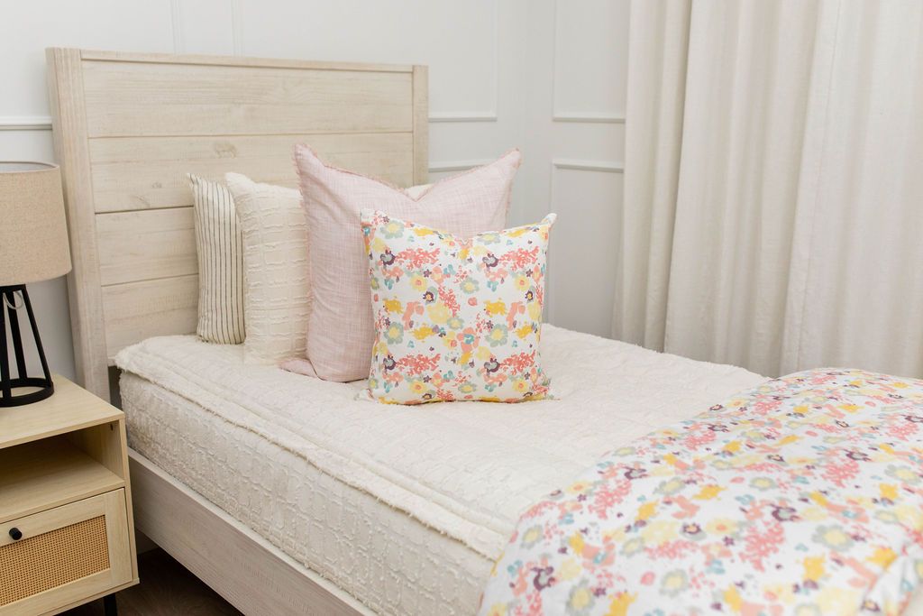 A close up view of a twin bed made with cream texture zipper bedding and pink and floral pattern pillows and a matching blanket.
