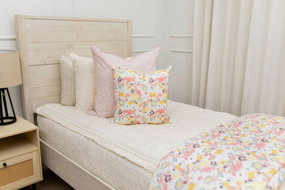 A close up view of a twin bed made with cream texture zipper bedding and pink and floral pattern pillows and a matching blanket.