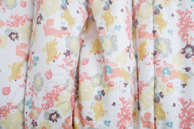 A close up of a blue, yellow, peach, and purple floral pattern blanket.