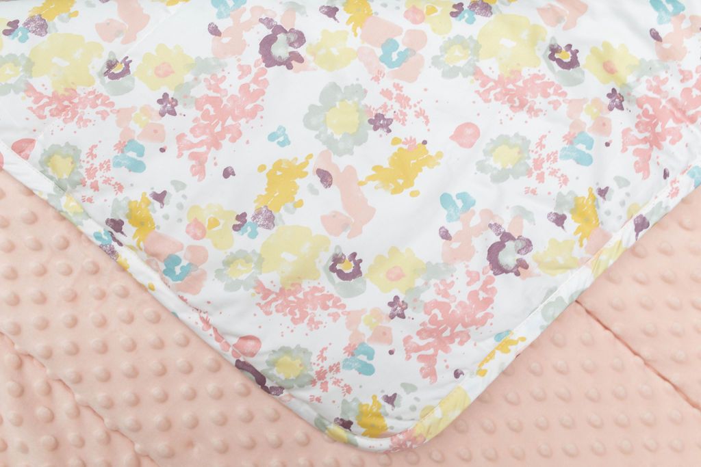 A close up of a blanket folded over to reveal the yellow, green, pink and purple floral design as well as showcase the pink minky underneath.