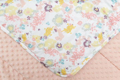 A close up of a blanket folded over to reveal the yellow, green, pink and purple floral design as well as showcase the pink minky underneath.