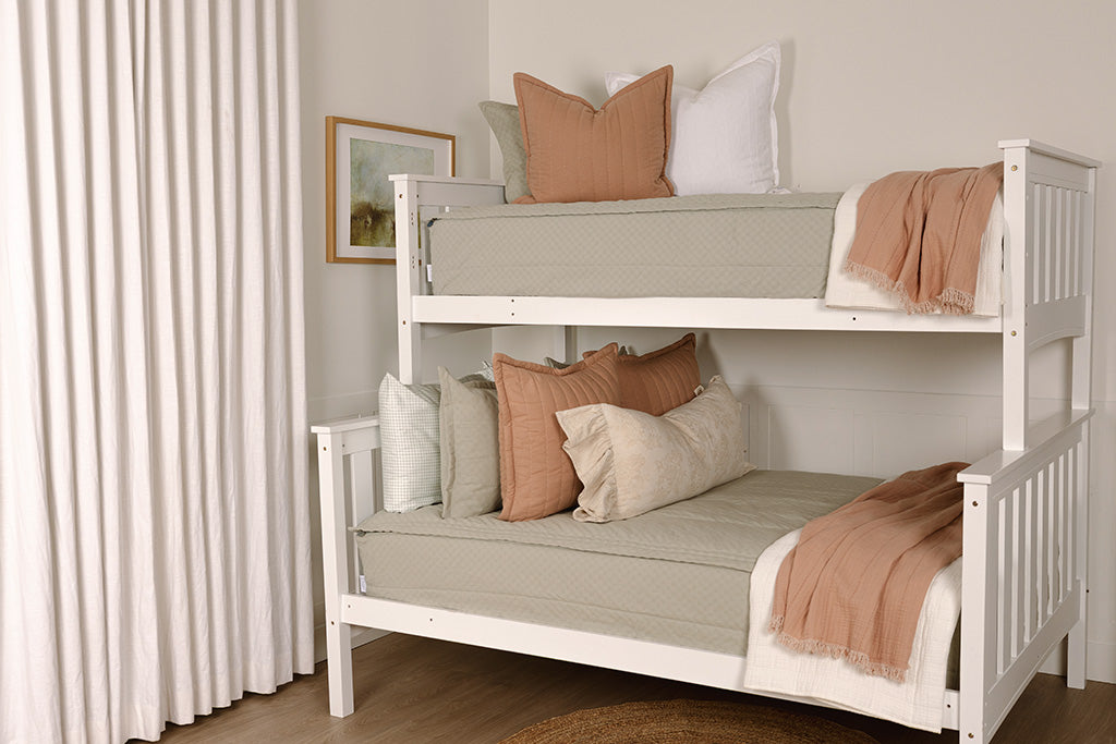 A bunk bed made with soft green zipper bedding and pink, white, and cream accessories. 