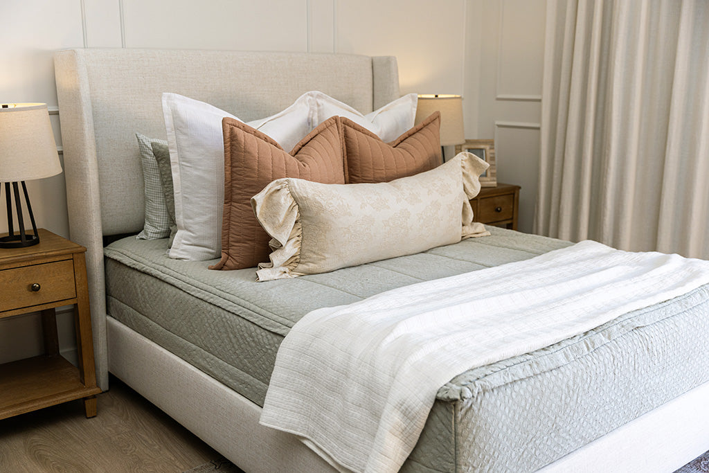 A queen bed made with soft green zipper bedding and pink, white, and cream accessories. 