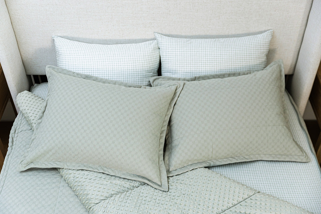 A bed made with honeycomb sage zipper bedding with the comforter pulled back and pillows on top of the bed.