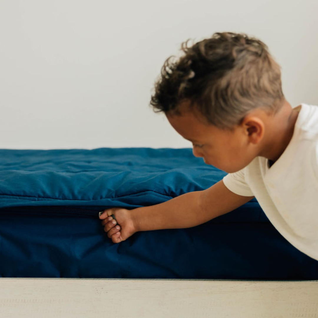 A young boy pulling the zipper closed on his navy blue zipper bedding set.
