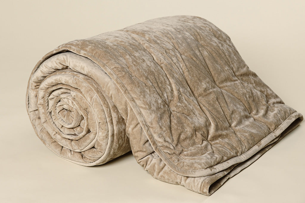 A tan velvet textured blanket rolled up on a cream backdrop.