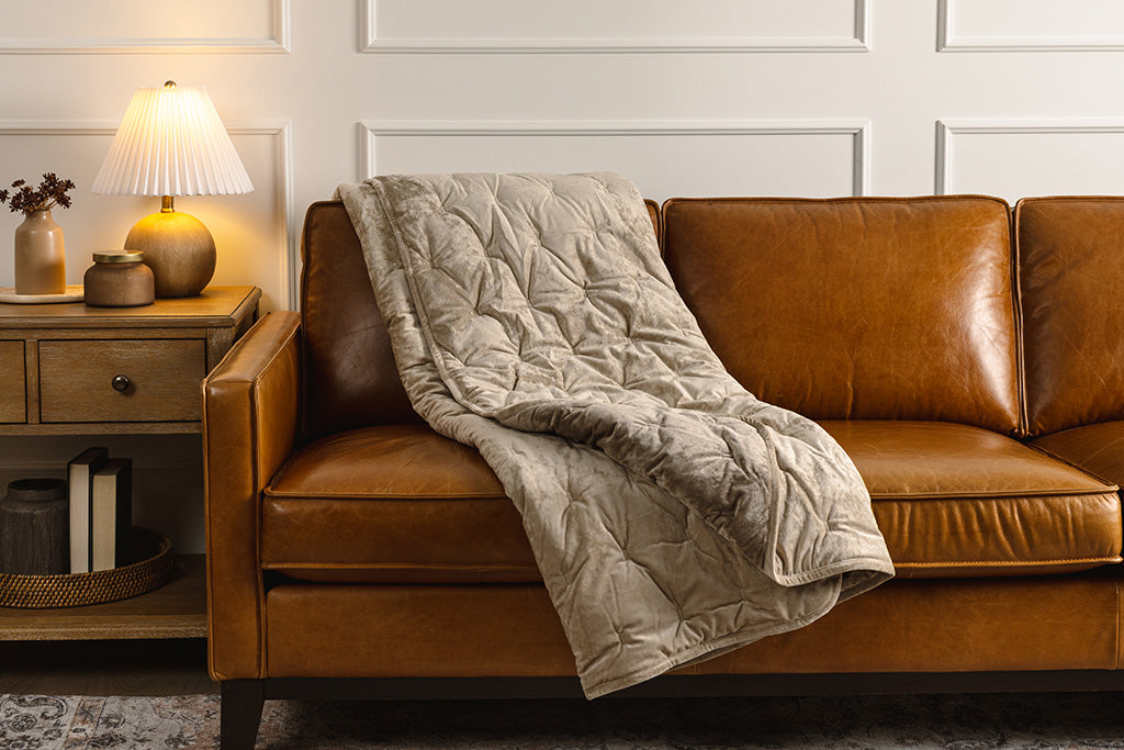 A tan velvet textured blanket placed on an orange leather couch.