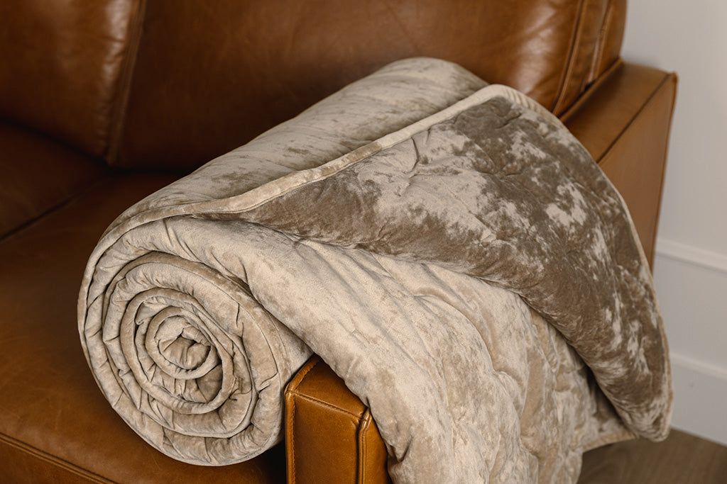 A tan and velvet textured blanket rolled up on an orange leather couch.