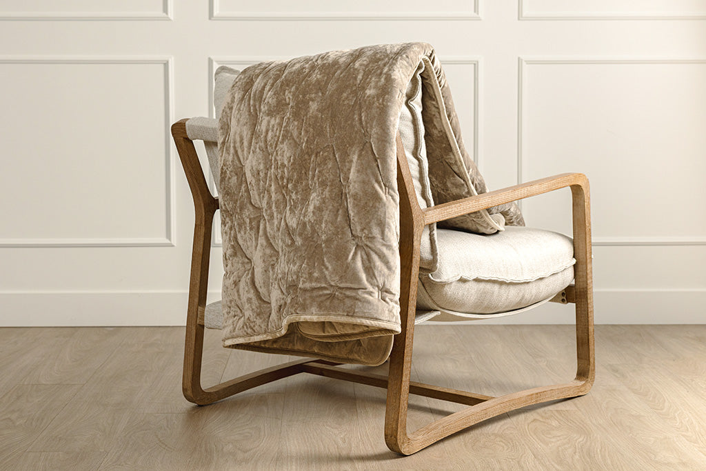 A tan and velvet textured blanket placed on a cream colored chair.