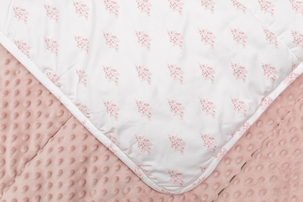 A close up of a white blanket folded over to reveal the pink floral design and underneath showcase the pink textured minky side. 