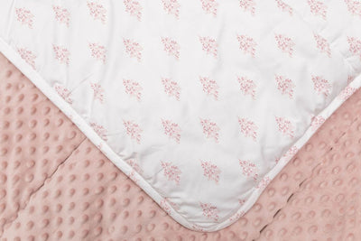 A close up of a white blanket folded over to reveal the pink floral design and underneath showcase the pink textured minky side. 