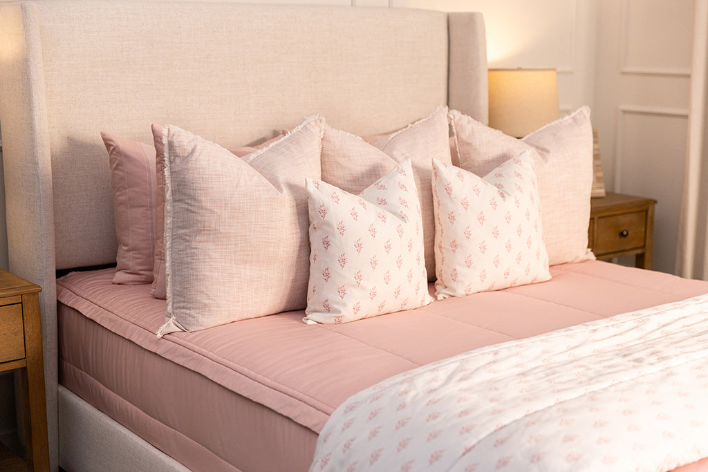 a bed made with pink zipper bedding with an assortment of pink and white bedding accessories