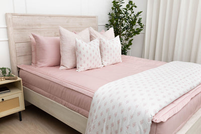 a bed made with pink zipper bedding with an assortment of pink and white bedding accessories