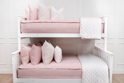 A standard bunk bed with both bunks made with pink zipper bedding and light pink and floral pillows and blankets.