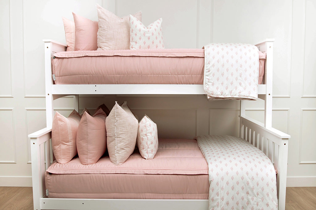 A standard bunk bed with both bunks made with pink zipper bedding and light pink and floral pillows and blankets.