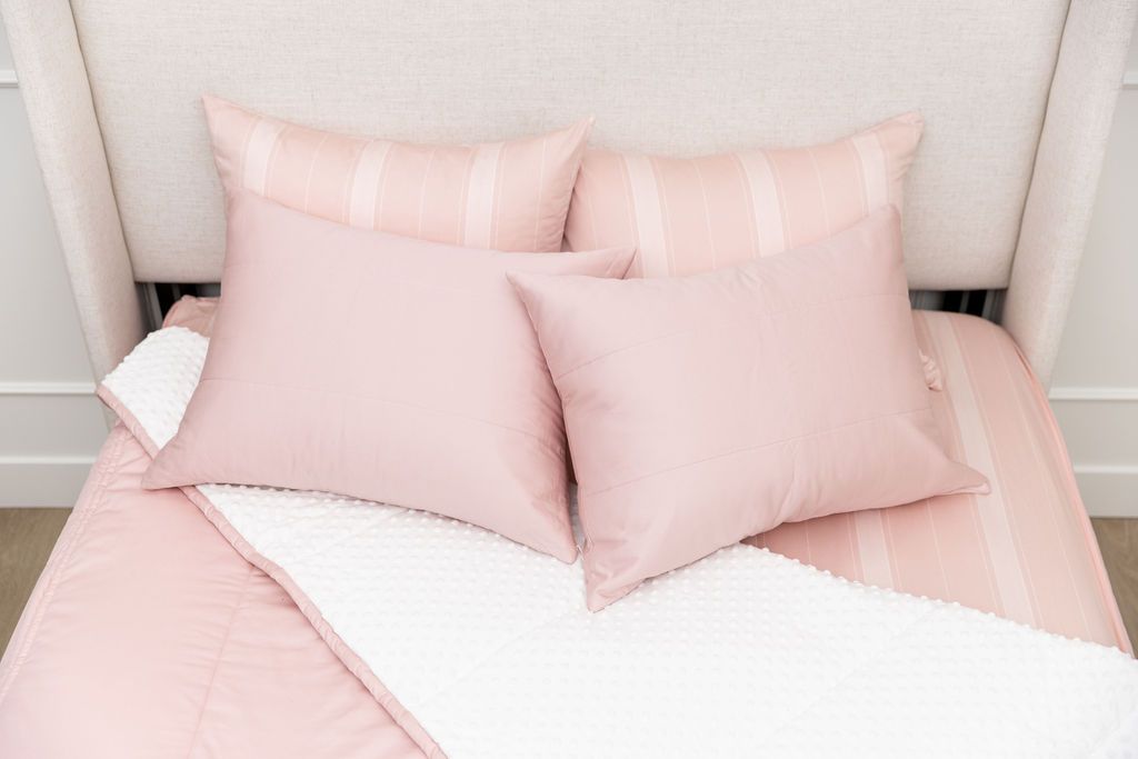 A bed made with pink zipper bedding with the comforter pulled back and pillows on top of the bed.