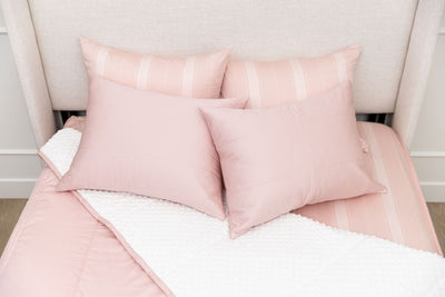 A bed made with pink zipper bedding with the comforter pulled back and pillows on top of the bed.