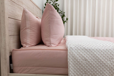 A side view of a bed made with pink zipper bedding with the top unzipped halfway down the bed and the comforter folded down.