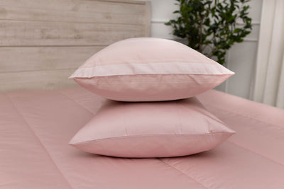 A pink striped pillowcase and matching sham on a made bed with pink zipper bedding. 