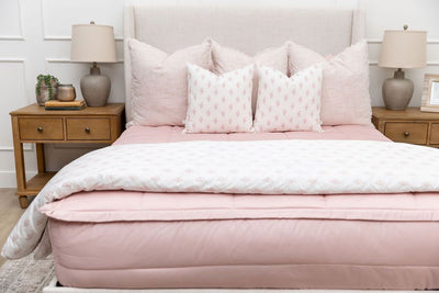 A bed made with pink zipper bedding and an assortment of light pink and floral pillows and blanket.