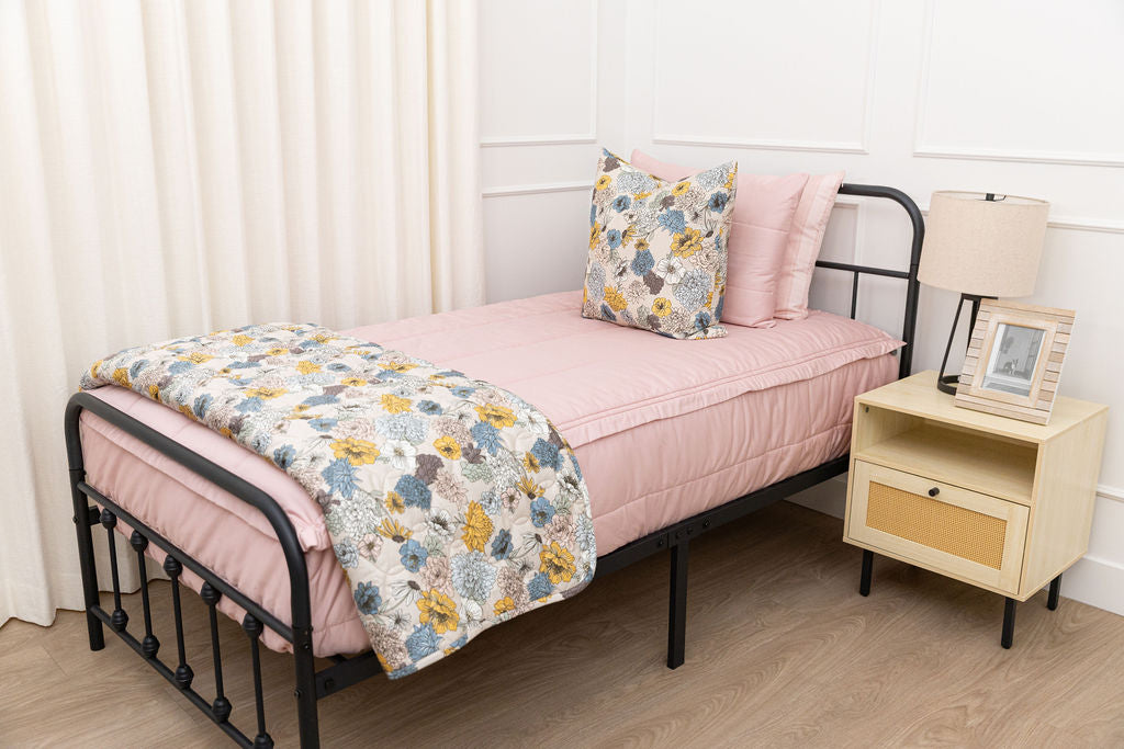 A twin bed made with pink zipper bedding and blue and yellow floral pillows and blanket.