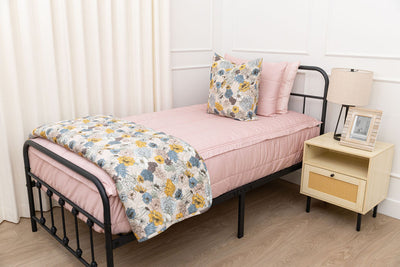 A twin bed made with pink zipper bedding and blue and yellow floral pillows and blanket.